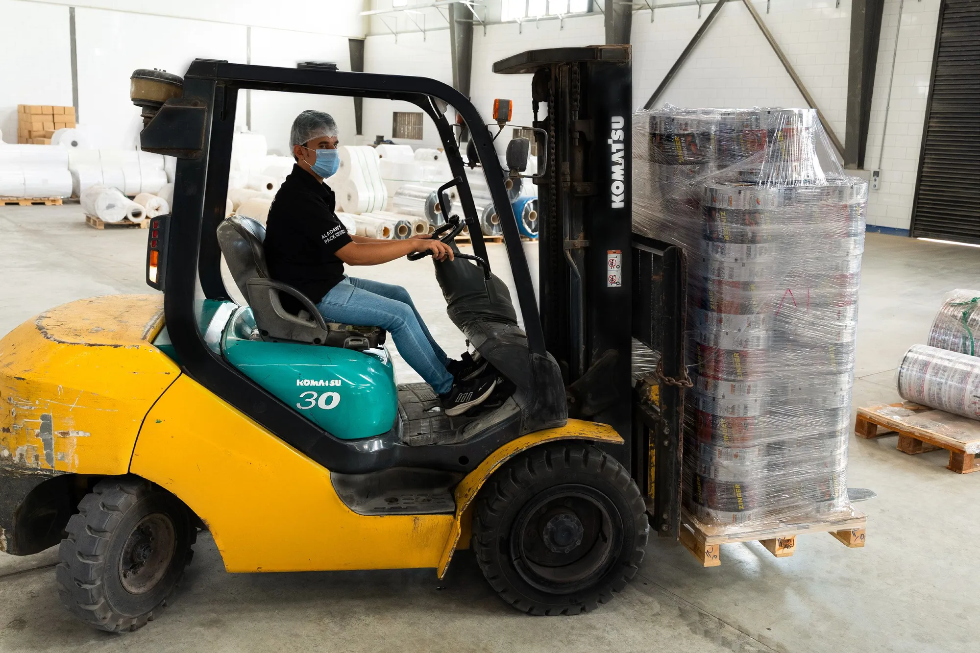 A forklift operator moving a wrapped pallet of film reels through the warehouse